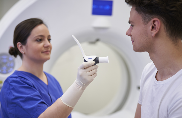 Eine medizinische Technologin für Radiologie reicht einem Patienten den Contrast Booster von ulrich medical für ein Lungenembolie-CT Untersuchung an. | © 2025 ulrich medical. Alle Rechte vorbehalten. Die Verwendung, Vervielfältigung oder Weitergabe ohne ausdrückliche Genehmigung ist nicht gestattet.