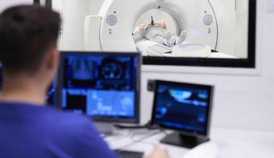 Sicht aus dem Kontrollraum in den Untersuchungsraum auf einem Patienten, bei dem ein Lungenembolie-CT mit dem Contrast Booster im Mund gemacht wird.